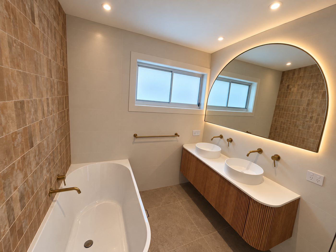 Renovated bathroom with freestanding bath, arched backlit mirror and timber double vanity
